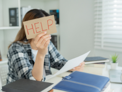 Person looking at paperwork holding a sign with the word Help.